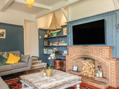A living room with a grey sofa cushions a wooden coffee table a brick fireplace firewood and a mounted TV at The Coach House in Teignmouth