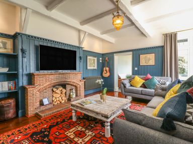 A living room with gray sofas and colorful cushions a wooden table a brick fireplace and a wall-mounted TV at The Coach House in Teignmouth