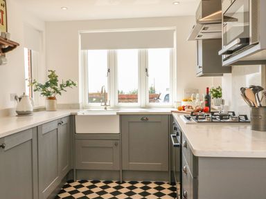 A kitchen with gray cabinets a white farmhouse sink a gas stove and checkered black and white floor at The Coach House in Teignmouth