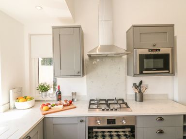 A kitchen with grey cabinets a gas stove a microwave and food on the counter at The Coach House in Teignmouth