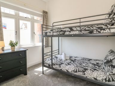 A bedroom with a bunk bed and a dark dresser beside a window at The Coach House in Teignmouth