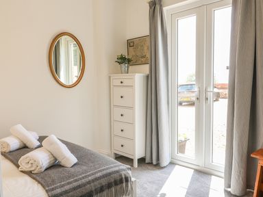 A bedroom with a bed, rolled towels, a chest of drawers, a round mirror, and glass door at The Coach House in Teignmouth