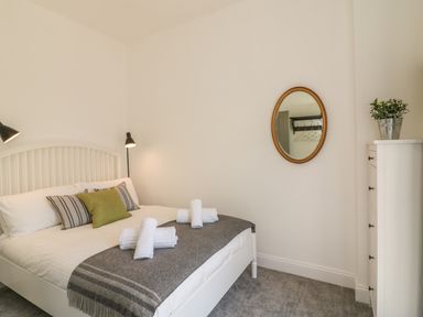 A bedroom with a bed with pillows and towels a dresser a mirror and a potted plant at The Coach House in Teignmouth