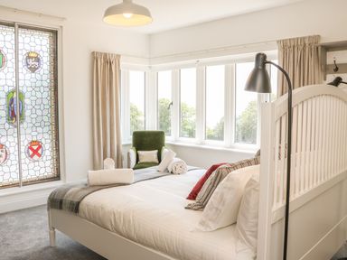 A bedroom with a white bed near a window with curtains and a green armchair at The Coach House in Teignmouth