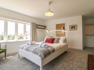 A bedroom with a white bed frame a window with curtains and a green chair at The Coach House in Teignmouth