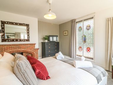 A bedroom with a bed pillow and a blanket near a window with stained glass and a cabinet with a television at The Coach House in Teignmouth