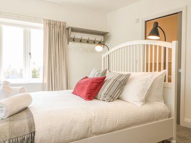 A bedroom with a white bed with striped and red pillows beside a window and wall hooks at The Coach House in Teignmouth