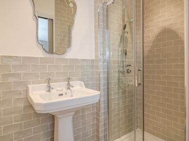 A bathroom with a pedestal sink a mirror above and a glass door shower at The Coach House in Teignmouth