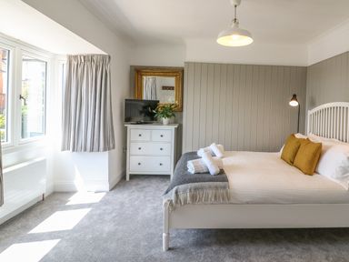 A bedroom with a white bed with mustard pillows and rolled towels a dresser with a TV and a mirror at The Coach House in Teignmouth