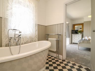 A bathroom with a freestanding bathtub a radiator and lace curtains next to a bedroom with a dresser a mirror and a bed at The Coach House in Teignmouth