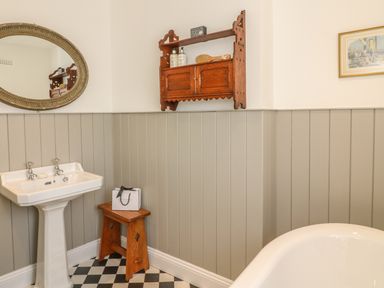 A bathroom with a pedestal sink a wooden stool a wall shelf and a bathtub at The Coach House in Teignmouth