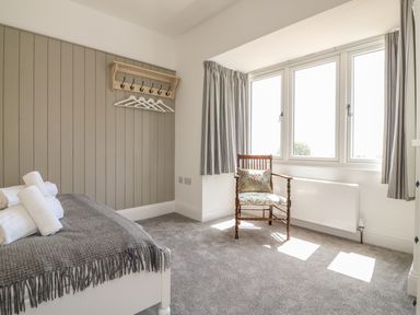 A bedroom with a bed with towels a wooden chair by windows and a wall-mounted coat rack at The Coach House in Teignmouth