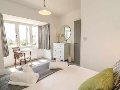 A bedroom with a bed with towels on it a wooden chair by the window and a white dresser with a round mirror at The Coach House in Teignmouth