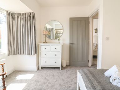 A bedroom with a gray door a white chest of drawers and a striped curtain at The Coach House in Teignmouth