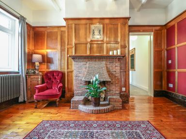 A room with wooden paneling a brick fireplace a red armchair a side table with a lamp and a plant on the fireplace at The Coach House in Teignmouth