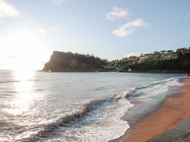A beach with small waves and a cliff with trees in the background at The Coach House in Teignmouth