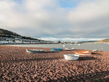 Boats on a sandy beach with houses on a hill in the background at The Coach House in Teignmouth