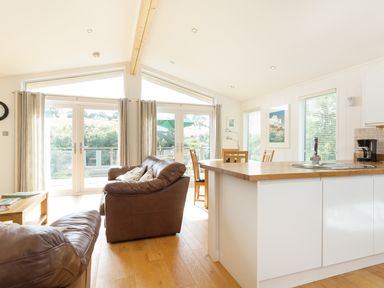 A living room with brown leather sofas a wooden table and an open kitchen area at 3 Valley View in Lanreath