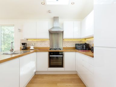 A kitchen with white cabinets wooden countertops a stainless steel oven and hood a coffee maker a microwave and a knife block at 3 Valley View in Lanreath