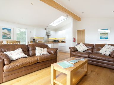 A living room with two brown leather sofas and a wooden coffee table in front of a kitchen with white cabinets at 3 Valley View in Lanreath
