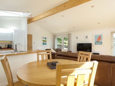 A kitchen and living room with a wooden dining table and chairs leather sofas a TV and framed pictures at 3 Valley View in Lanreath