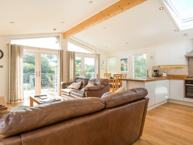 An open plan living room and kitchen with brown leather sofas wooden dining table and white kitchen cabinets at 3 Valley View in Lanreath