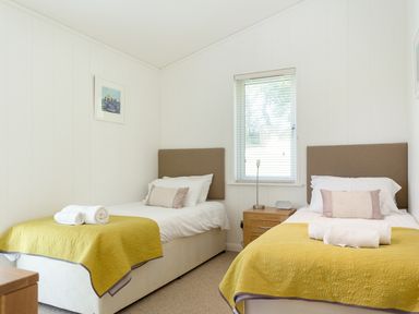 A bedroom with two single beds with yellow blankets and white towels on them a window with blinds and a bedside table with lamp at 3 Valley View in Lanreath