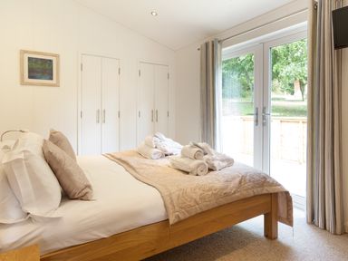 A bedroom with a wooden bed, rolled towels on the bed, white wardrobes, and glass doors with curtains at 3 Valley View in Lanreath