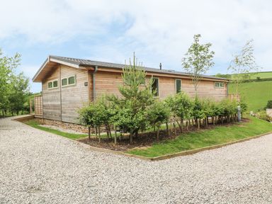 A wooden building with small trees and shrubs along a gravel pathway at 3 Valley View in Lanreath