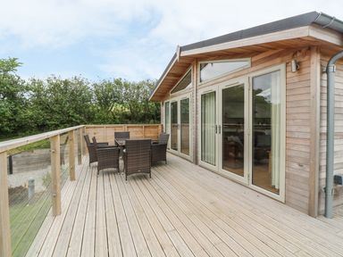 A wooden deck with glass railing and outdoor dining set next to a building with glass doors at 3 Valley View in Lanreath