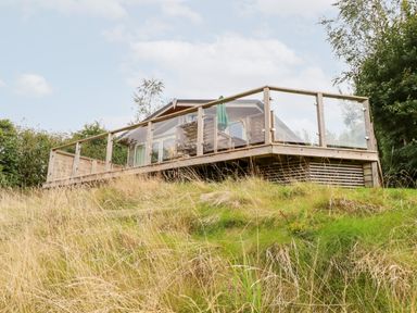A wooden deck with glass railings and outdoor furniture on a grassy hill at 3 Valley View in Lanreath