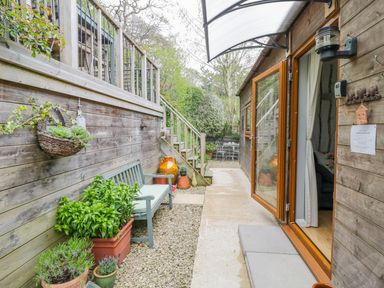 A narrow outdoor patio with potted plants, a bench, wooden stairs, and an open glass door at Wellinghill Lodge in Cheltenham
