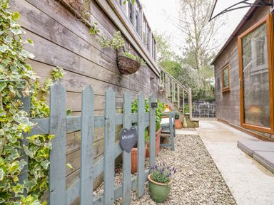 A gravel pathway with a wooden gate and potted plants between two wooden buildings at Wellinghill Lodge in Cheltenham
