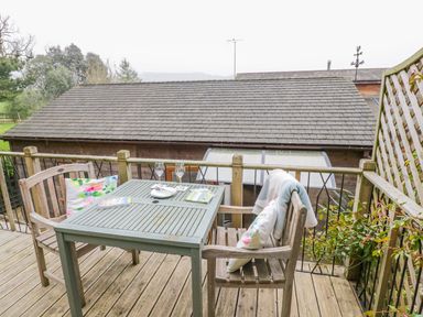 An outdoor wooden deck with a table and two chairs with cushions and a blanket at Wellinghill Lodge in Cheltenham