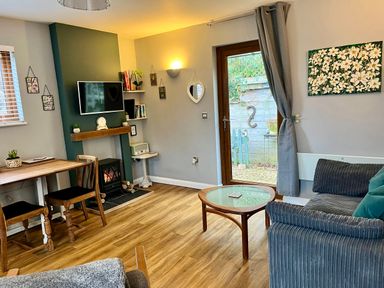 A living room with a wooden dining table and chairs a sofa and coffee table a fireplace with a mounted TV and a door leading outside at Wellinghill Lodge in Cheltenham