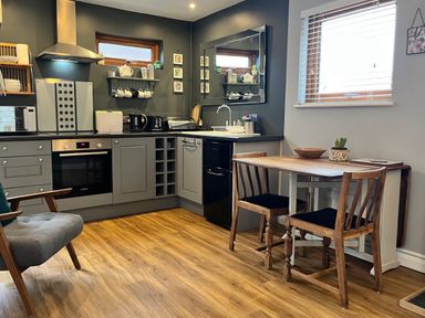 A kitchen with grey cabinets a black countertop and wooden dining table with two chairs at Wellinghill Lodge in Cheltenham