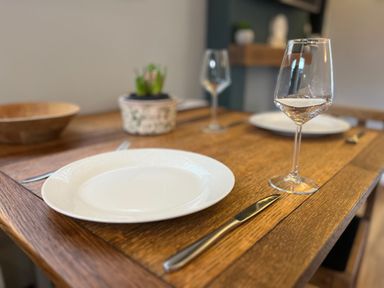 A wooden dining table set with white plates, wine glasses, knives, forks, and a small potted plant at Wellinghill Lodge in Cheltenham