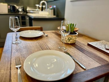 A wooden dining table set with two white plates knives forks and wine glasses with a small plant in a decorative pot on the table at Wellinghill Lodge in Cheltenham