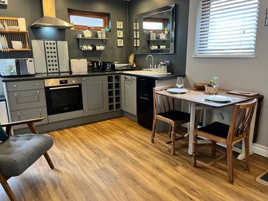 A kitchen with gray cabinets wooden floor and a dining table with two wooden chairs at Wellinghill Lodge in Cheltenham