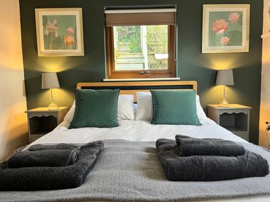 A bedroom with a bed with green pillows and gray towels on a blanket at Wellinghill Lodge in Cheltenham