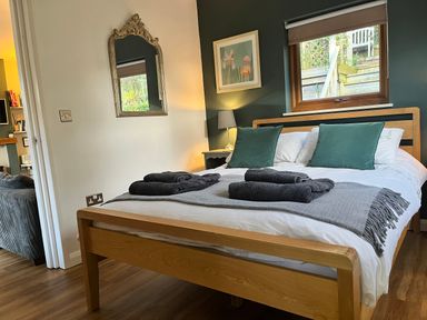 A bedroom with a wooden bed frame cushions and folded towels on the bed at Wellinghill Lodge in Cheltenham