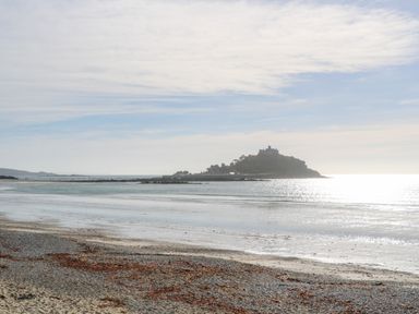 A beach with seaweed and pebbles on the shore and a small island with a castle in the background at The Stables in Longrock