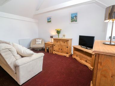A living room with a beige sofa a round chair wooden cabinets a television and wall art at The Stables in Longrock