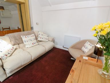 A sitting area with a beige sofa and armchair with patterned cushions and a wooden table with yellow flowers at The Stables in Longrock