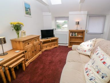 A living room with wooden furniture a television a beige sofa with patterned cushions and red carpet at The Stables in Longrock