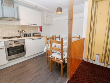 A kitchen with a stove oven white cabinets and a dining table with wooden chairs at The Stables in Longrock
