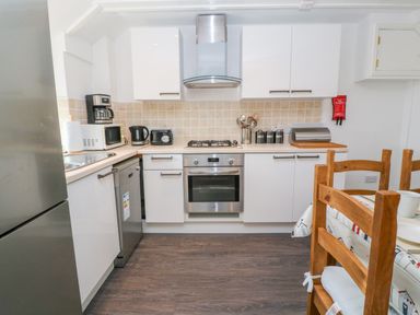 A kitchen with white cabinets a stainless steel oven stovetop dishwasher and refrigerator and wooden chairs at The Stables in Longrock