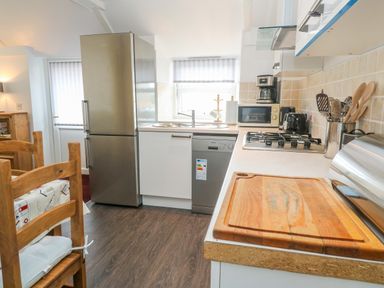 A kitchen with wooden chairs a stainless steel fridge dishwasher gas stove and wooden cutting board at The Stables in Longrock