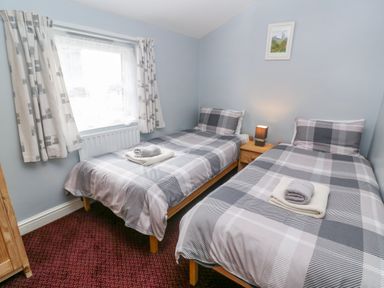 A bedroom with two single beds a nightstand with lamp and a window at The Stables in Longrock