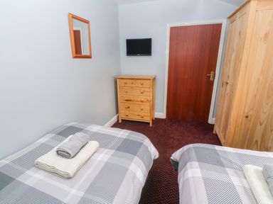 A bedroom with two single beds with folded towels on top a wooden chest of drawers a wall-mounted TV a wooden wardrobe a mirror and a closed wooden door at The Stables in Longrock